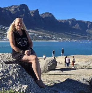 Linda Khanna, WOW Director and host, seated on rocks above a bay in South Africa
